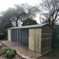 Load image into Gallery viewer, KENNELSTORE Wymbury Double Wooden Dog Kennel, a 18ft x 5ft multi-dog housing unit. The kennel features a distinctive apex roof and is made from pressure-treated tanalised timber, with two separate runs equipped with galvanised panels for security.