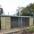 Load image into Gallery viewer, KENNELSTORE Wymbury Double Wooden Dog Kennel, a 21ft x 5ft multi-dog housing unit. The kennel features a distinctive apex roof and is made from pressure-treated tanalised timber, with two separate runs equipped with galvanised panels for security.