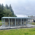 Load image into Gallery viewer, A multi-unit wooden dog kennel block with multiple runs. The structure is built with pressure-treated timber and features galvanized steel bar panels for the runs, with each unit having a separate, enclosed sleeping area. The kennel is designed for multiple dogs and is durable and secure.
